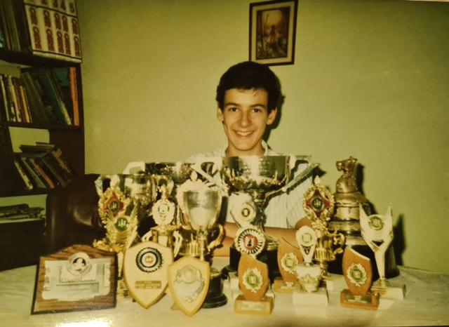 A person sitting behind a table with trophies
Description automatically generated